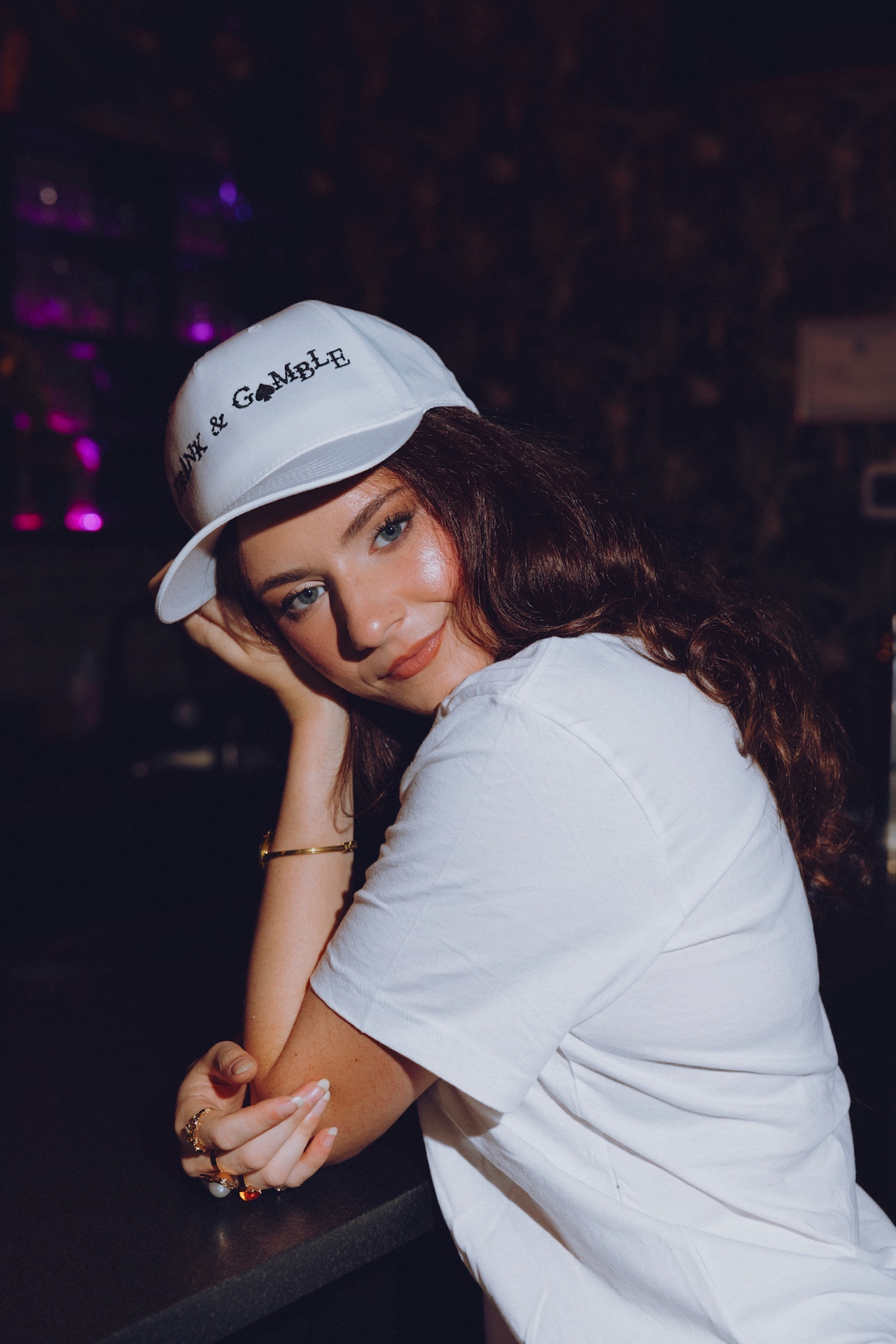 Brunette in a white Drink & Gamble cap leaning on the bar